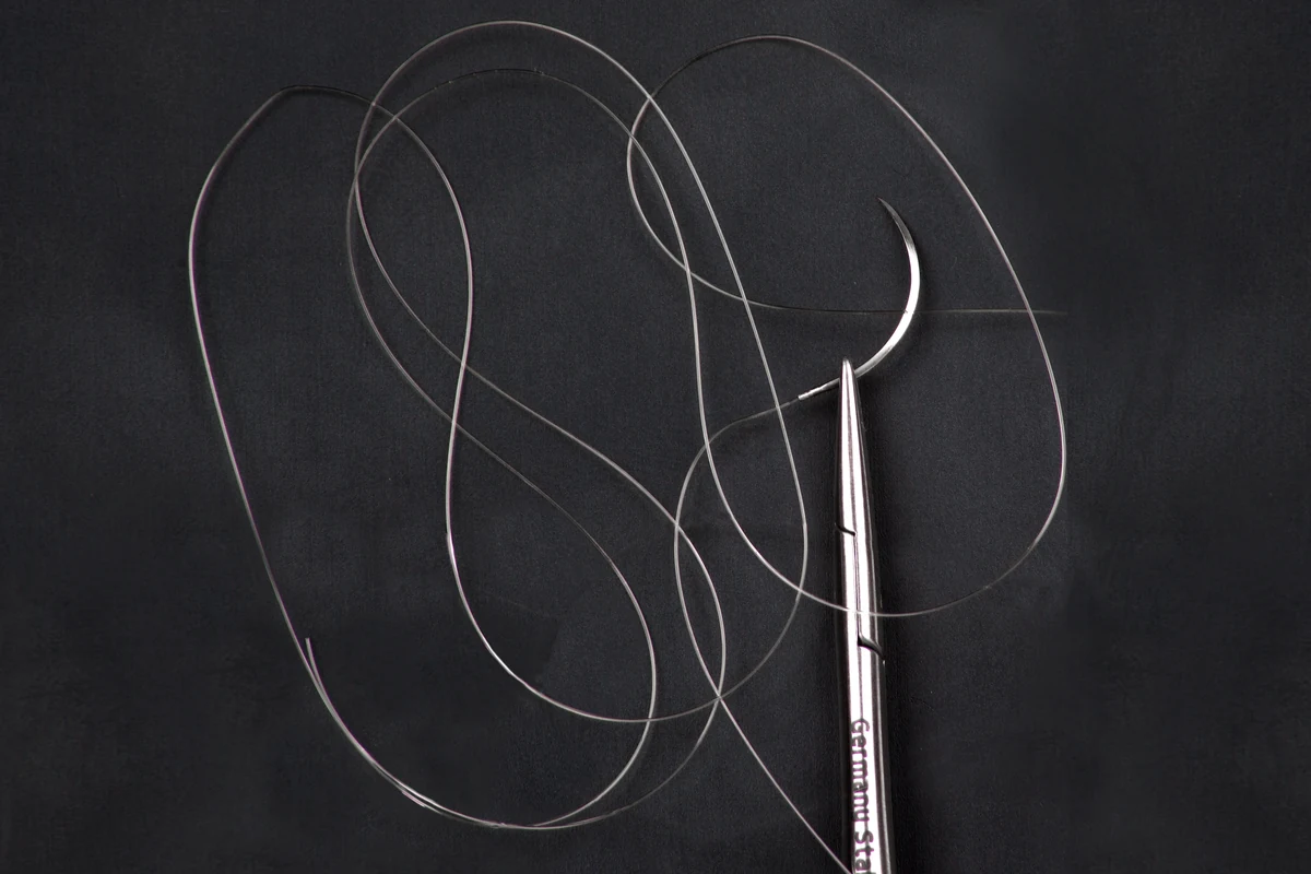 Ago chirurgico VITREX con filo di sutura in PTFE trasparente su fondo nero